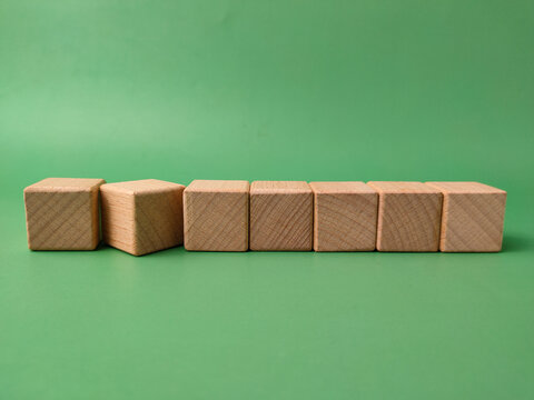 The image displays seven natural, unfinished wooden cubes arranged in a line on a green background