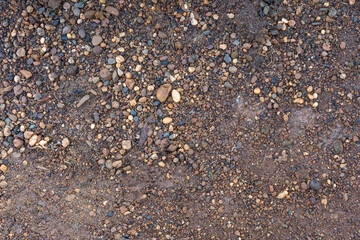 Brown dirt and small multicolored rounded pebbles forming a rough textured ground surface background