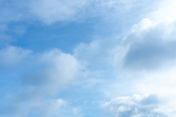 Bright light illuminates scattered white and gray cumulus clouds across a vast pale blue sky
