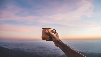 Hand Holds Orange Coffee Mug Up To Misty Mountain Cityscape Under Pink and Blue Sunset Sky Majestic Mountain View with Soft Clouds and Foggy Valley Below Calm Serene Atmosphere
