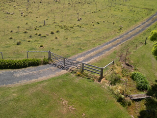 Aerial view of rural farm gate and gravel driveway in open green countryside