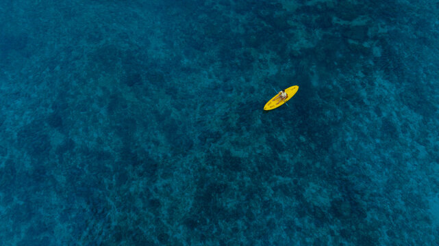 Aerial view woman bright yellow kayak with in the vast expanse of crystal clear turquoise water. The seabeds rocky texture is visible beneath the surface, concept marine environment - Powered by Adobe