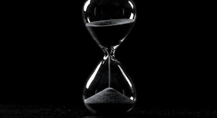 Hourglass against a black background. Close-up of a transparent sand timer with flowing sand