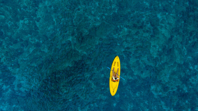Aerial view woman bright yellow kayak with in the vast expanse of crystal clear turquoise water. The seabeds rocky texture is visible beneath the surface, concept marine environment - Powered by Adobe