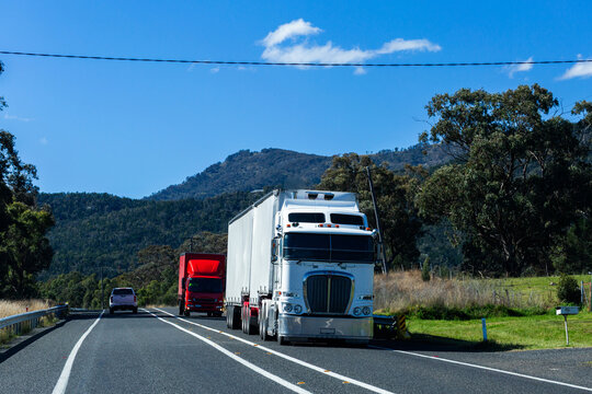 Semi-trailer trucks travelling on country road in Australia in bright sunlight near Moonbi