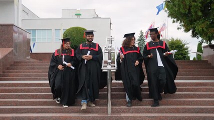 Diverse graduates walking down university stairs after ceremony - Powered by Adobe