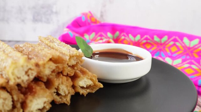 A plate of churros rotates next to a bowl of chocolate and a mint leaf. Mexican food