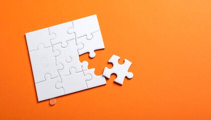 White jigsaw puzzle with one piece detached on bright orange background. High angle shot with copy space