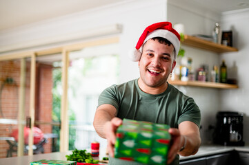 A cheerful man in a santa hat holds a colourful gift, celebrating the holiday spirit at home