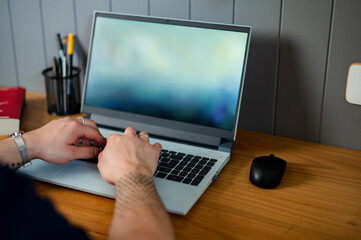 a crop shot of a man typing in a laptop in a stylish home office.