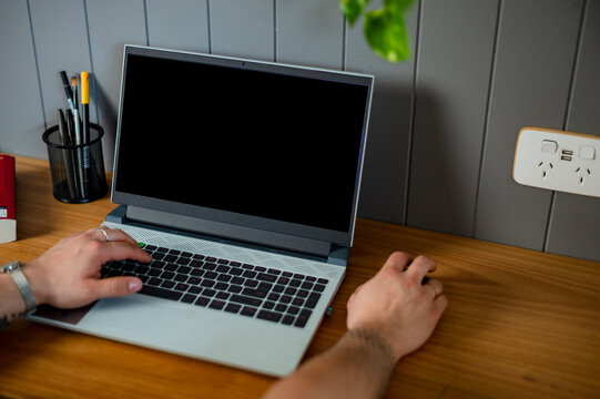 A crop shot of a man seated at his home office desk, using a laptop