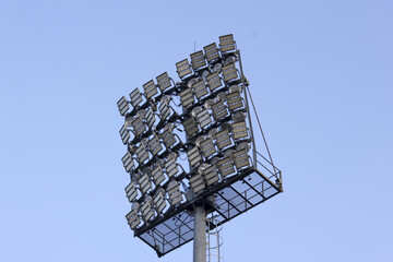 Powerful stadium floodlight tower with large lighting system of lamps against clear blue sky, ready to illuminate field for an exciting evening sport event