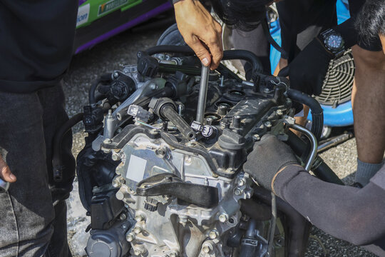 Concentrated mechanic fixing car engine with tool. People work on automobile motor for repair and maintenance service in garage. Focused teamwork on vehicle