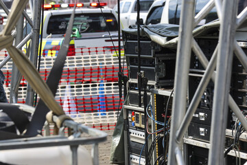 Backstage event setup with professional sound system, audio equipment, speaker, and metal rigging. An emergency vehicle in background during concert preparation
