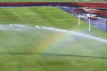 Obraz premium Tranquil sprinkler system watering lush green grass soccer field, vibrant rainbow visible in spray. irrigation process maintains wet pitch for an upcoming game