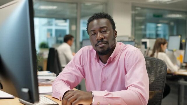 Focused Professional at Work: A poised individual, dressed in a business casual shirt, sits at a desk in a modern office. His expression is one of focus and determination.