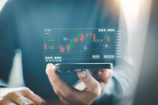 Businessman holding smartphone with holographic stock market graph. Fintech concept showing financial investment, crypto trading analysis, and digital economy growth on mobile device.