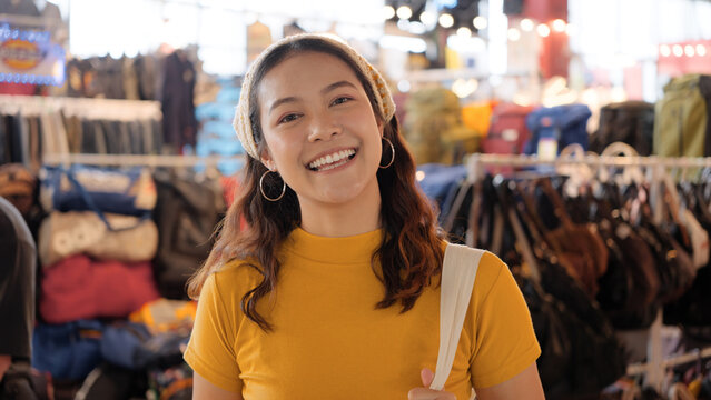 Young teen Gen Z asia female happy smile looking at camera at zero waste eco go green buy second hand sale store flea market mall thrift old used vintage fabric retro style. Woman people enjoy shop.