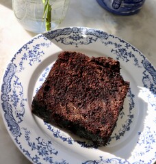Coffee and chocolate cake with white rose in little vase on blue tableware with sunlight