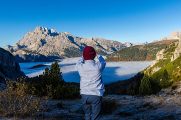 A senior traveler hikes alone along a mountain trail under bright sunlight, surrounded by stunning...
