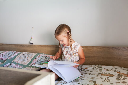 Little preschool aged child sitting on bunk bed reading a storybook looking at pictures in bedroom