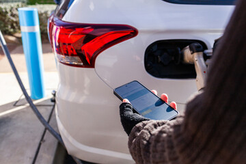 Person holding phone to use app for charging hybrid car at public charger