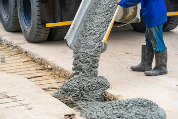 Nonthaburi, Thailand - November, 07, 2025 : Construction workers pouring wet concrete from a truck chute and spreading it using tools for a pavement or foundation