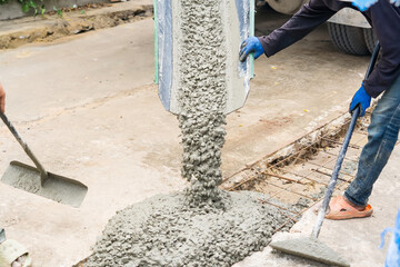 Nonthaburi, Thailand - November, 07, 2025 : Construction workers pouring wet concrete from a truck chute and spreading it using tools for a pavement or foundation