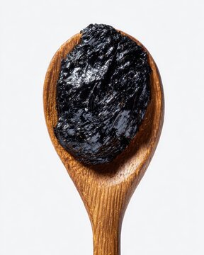 High-detail macro shot of thick black shilajit resin on wooden spoon, glossy surface catching light, minimal white studio background, perfect for herbal supplement photography.