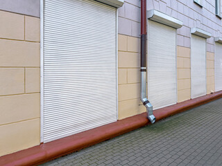 building facade with row of windows with closed roller shutters and rainwater downspout.