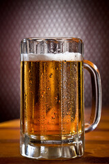 A large mug of cold beer and frost on a wooden table and black background. 