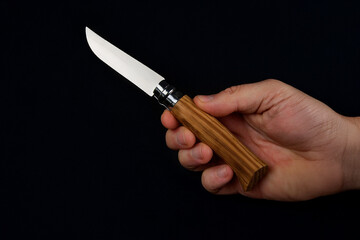 A timeless classic folding knife featuring a polished bright blade and a beautifully grained wooden handle held in hand