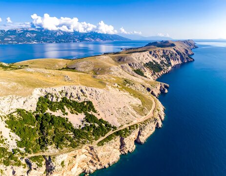 Aerial view captures a sun-drenched, rocky peninsula extending into a vibrant blue sea, with a distant mountain range