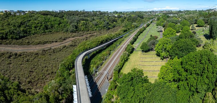 Aerial view of a pedestrian bridge, railway tracks, and cemetery in Meadowbank, Auckland, New Zealand. The bridge allows people to cross over the railway and wetlands, providing access to nature.