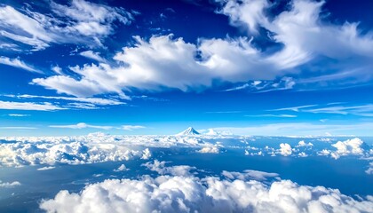 Stunning aerial view showcasing a bright blue sky filled with puffy white clouds, with a snow-capped mountain peak peeking through