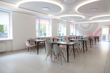 Tables with chairs in stylish room at school