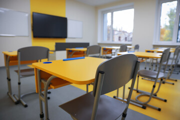 Stylish classroom with desks, chairs and tv at school, selective focus