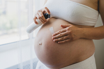 A pregnant woman applies skincare cream to her skin. This moment emphasizes self-care during pregnancy.
