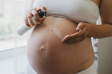 A pregnant woman applies skincare cream to her skin. This moment emphasizes self-care during pregnancy.