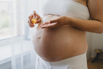 A pregnant woman applies skincare cream to her skin. This moment emphasizes self-care during pregnancy.