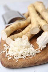 Grated horseradish, grater and fresh roots on white table, closeup
