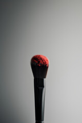 Soft makeup brush coated with vibrant red powder against a dark background