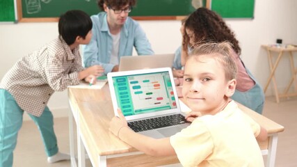 Cute caucasian boy coding program and looking at camera in STEM technology class while group of diverse student and teacher doing mind mapping. Smart child learning coding software program. Pedagogy. - Powered by Adobe