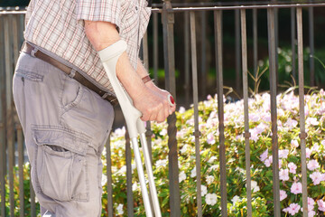 Mature adult male with crutches moving along a fence, needing assistance for mobility and...