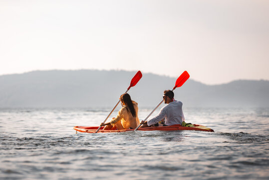 Young couple of tourists are relaxing and kayaking at sunset sea bay