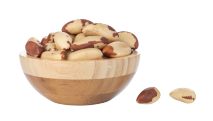 A wooden bowl filled with several brazil nuts, and two more brazil nuts are next to the bowl, all on a white surface cutout