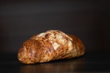 Freshly baked golden croissant resting on a dark wooden surface, showcasing flaky layers and a buttery texture, perfect for breakfast or pastry lovers