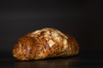 Freshly baked golden croissant resting on a dark wooden surface, showcasing flaky layers and a buttery texture, perfect for breakfast or pastry lovers