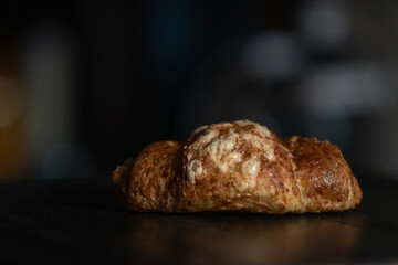 Freshly baked golden croissant resting on a dark wooden surface, showcasing flaky layers and a buttery texture, perfect for breakfast or pastry lovers