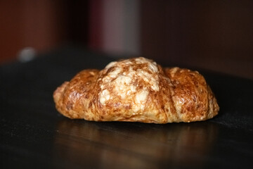 Freshly baked golden croissant resting on a dark wooden surface, showcasing flaky layers and a buttery texture, perfect for breakfast or pastry lovers